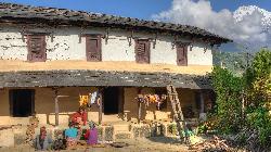 Household chores being done in the courtyard of the typical Gurung house, at the right rises Annapurna South out of the morning clouds.