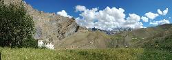 Panorama with large house and puffy white clouds in the dark blue afternoon sky.